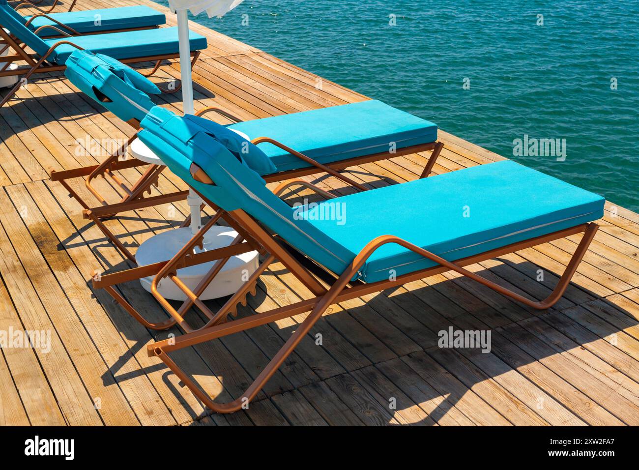 Groupe de chaises longues de luxe sur une jetée en bois en attente pour les touristes dans une chaude journée d'été. Voyage, tourisme, loisirs et concept de vacances. Banque D'Images