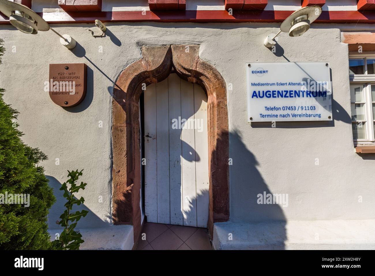 Un portail en arc brisé gothique tardif mène à un bâtiment sur la place du Kaufhaus à Altensteig, dans la vieille ville d'Altensteig, en Bade-Wurtemberg, en Allemagne. Une plaque date la maison de 1527–1697 en tant qu'hôpital municipal (Bürgerspital), avec une section en colombage de style baroque ajoutée en 1612. Il abrite aujourd'hui la clinique oculaire Augenzentrum du cabinet Medizentrum Eckert. Banque D'Images