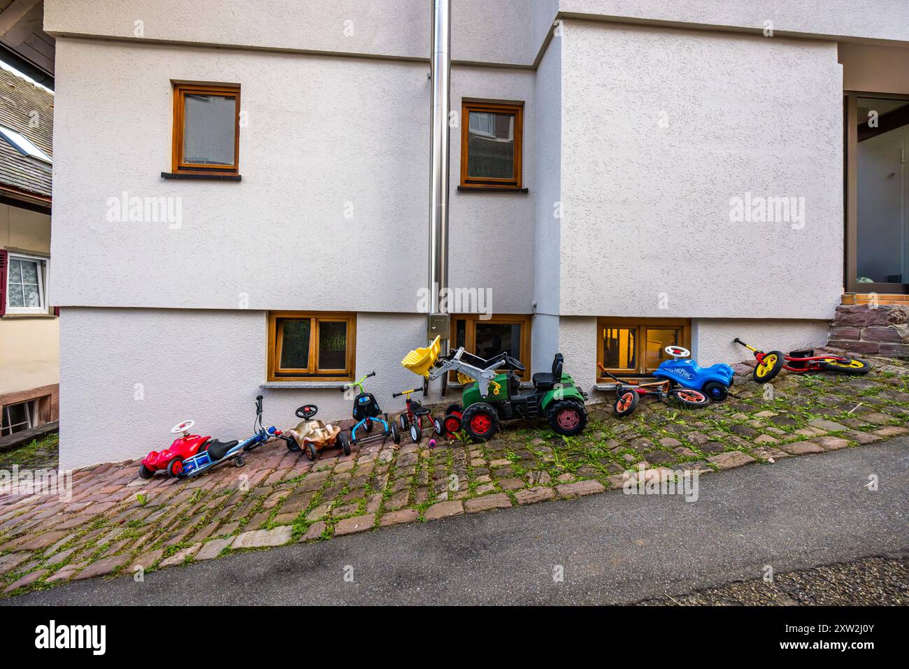 Des vélos à pédales et des vélos d’équilibre pour enfants sont alignés contre un mur de maison sur la Kirchgasse à Berneck, Altensteig, Baden-Württemberg, Allemagne. Banque D'Images