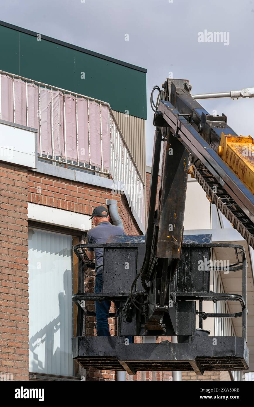 homme avec un chapeau noir sur la tête se tient dans une boîte en métal d'une plate-forme de travail aérienne Banque D'Images