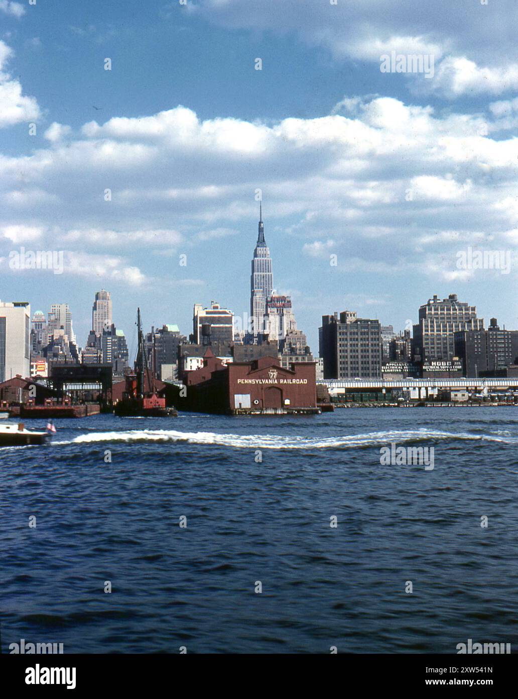 New York, États-Unis. Septembre 1959 : vue du Pier 77, le quai de fret du Pennsylvania Railroad, prise depuis la rivière Hudson, New York. Visible au loin, vous trouverez le New Yorker Hotel et l'Empire State Building. Un grand panneau publicitaire est affiché sur le bâtiment Hobb Electrical Supply Corp, situé aux 34e et 35e rues. Banque D'Images