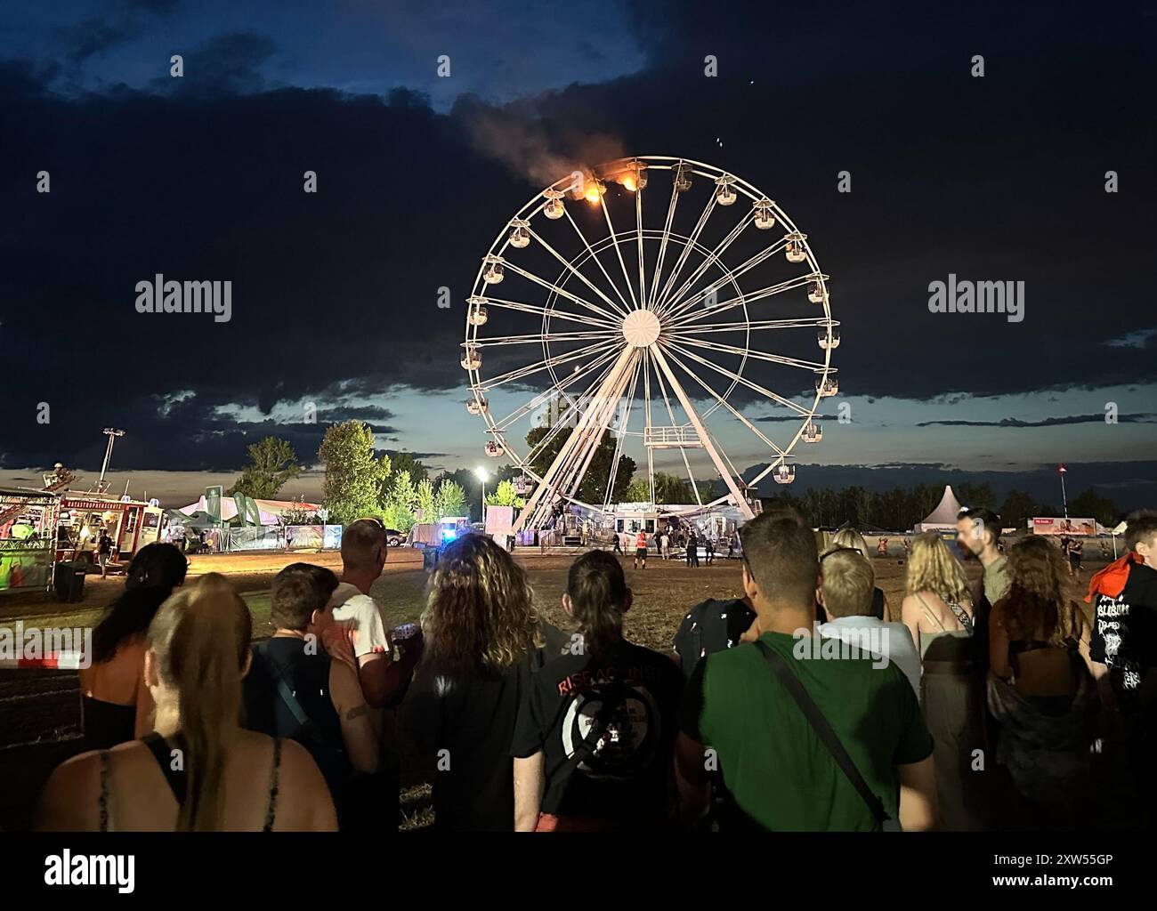 17 août 2024, Saxe, Großpösna : les visiteurs du Highfield Festival regardent une grande roue sur laquelle des flammes peuvent être aperçues. Un incendie s'est déclaré sur une grande roue au Highfield Festival sur le lac Störmthal. Photo : Str./dpa Banque D'Images