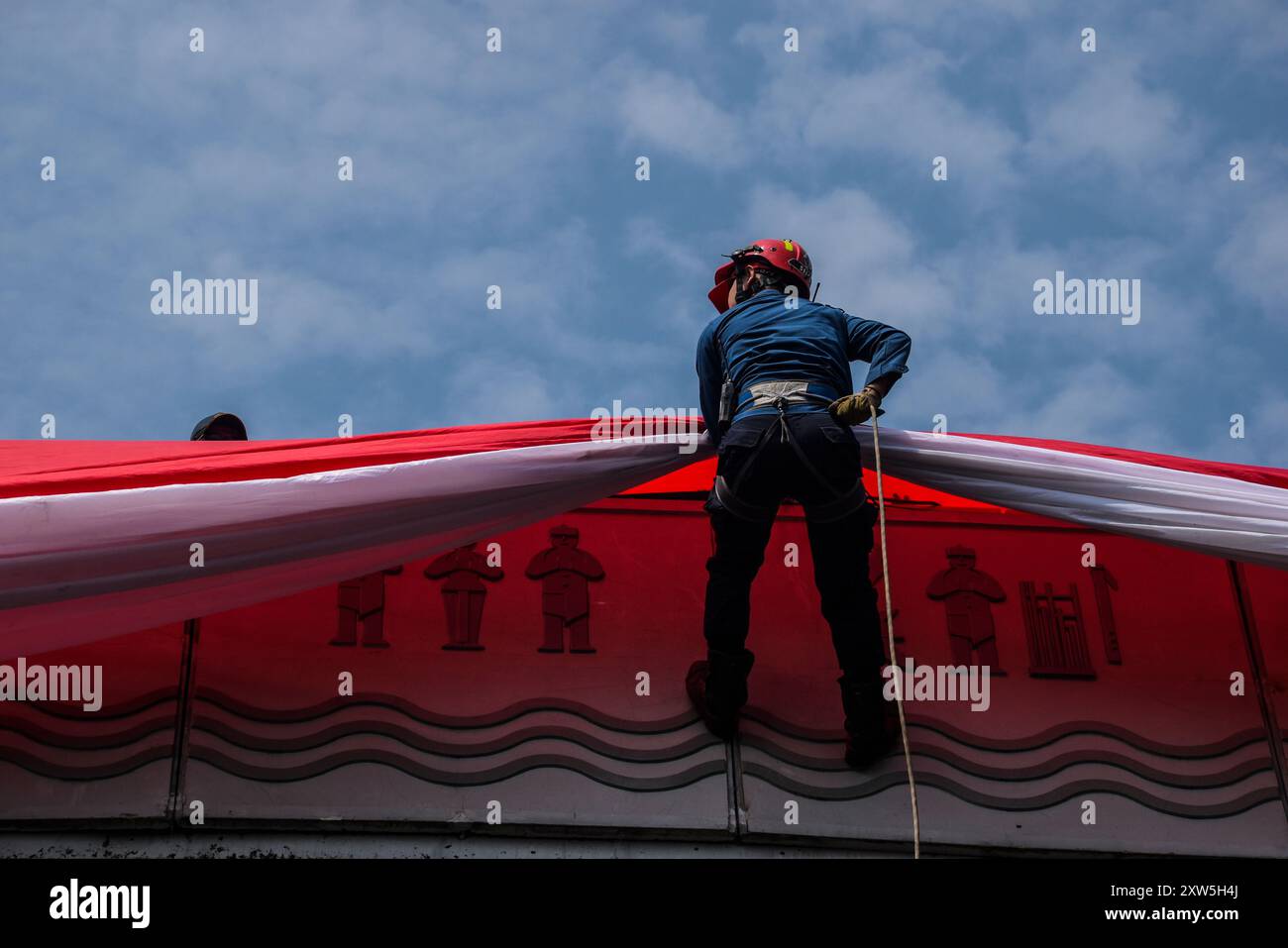 Bandung, Indonésie. 17 août 2024. Un pompier descend d'un pont pour hisser un drapeau rouge et blanc géant lors d'un salut de trois minutes commémorant le 79e jour de l'indépendance de la République d'Indonésie à Bandung, Java occidental. (Photo de Dimas Rachmatsyah/Pacific Press) crédit : Pacific Press Media production Corp./Alamy Live News Banque D'Images