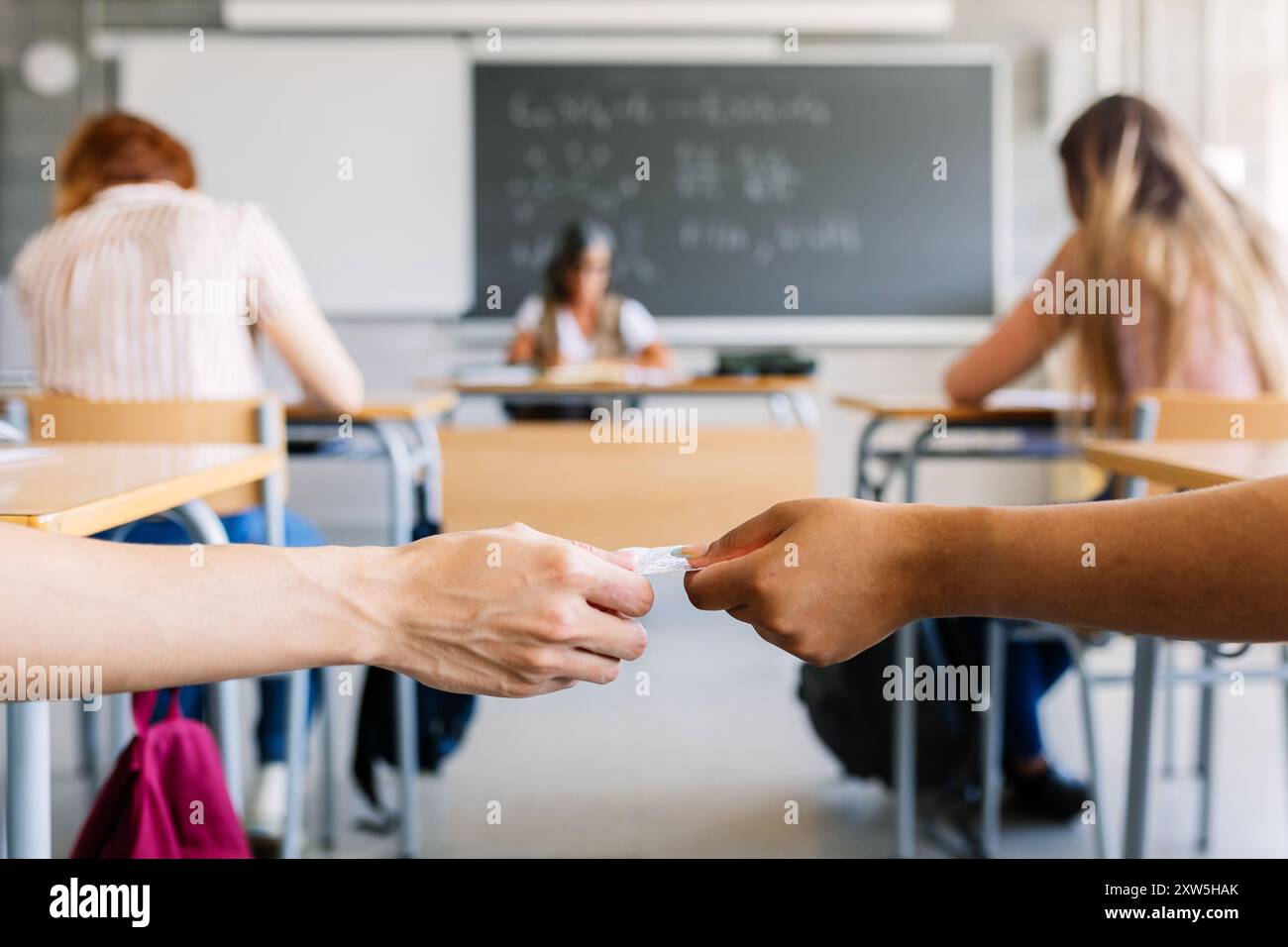 Lycéen donnant une feuille de triche à un camarade de classe pendant l'examen en classe Banque D'Images