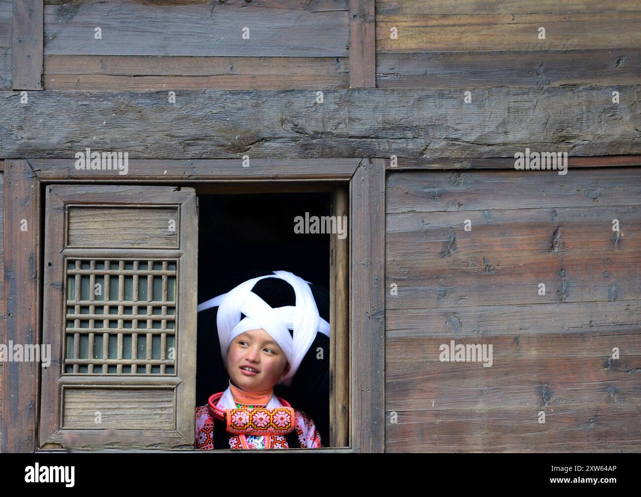 Une adolescente Miao à longue corne regardant par sa fenêtre pendant le festival Tiao Hua / printemps dans la province du Guizhou, en Chine. Banque D'Images