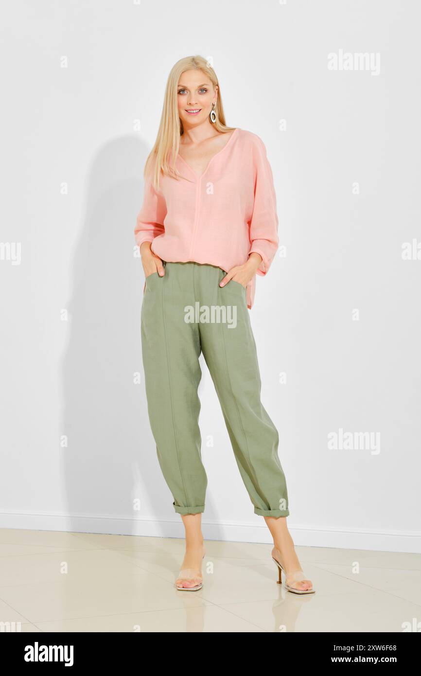 Femme élégante aux cheveux blonds lisses portant une blouse rose et un pantalon vert ample Banque D'Images