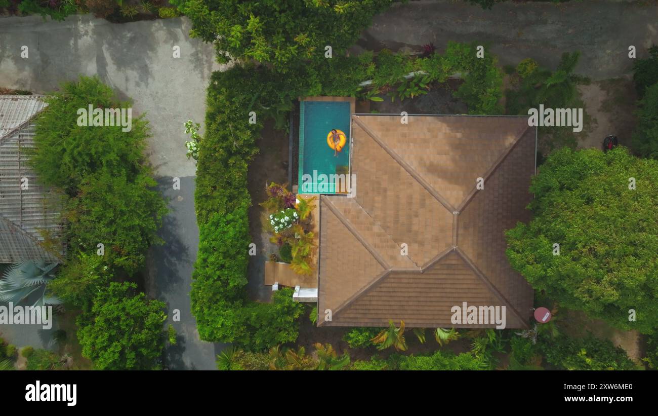 Vue aérienne d'une femme profitant de ses vacances flottant sur un anneau gonflable jaune dans une piscine dans une villa de luxe tropicale Banque D'Images