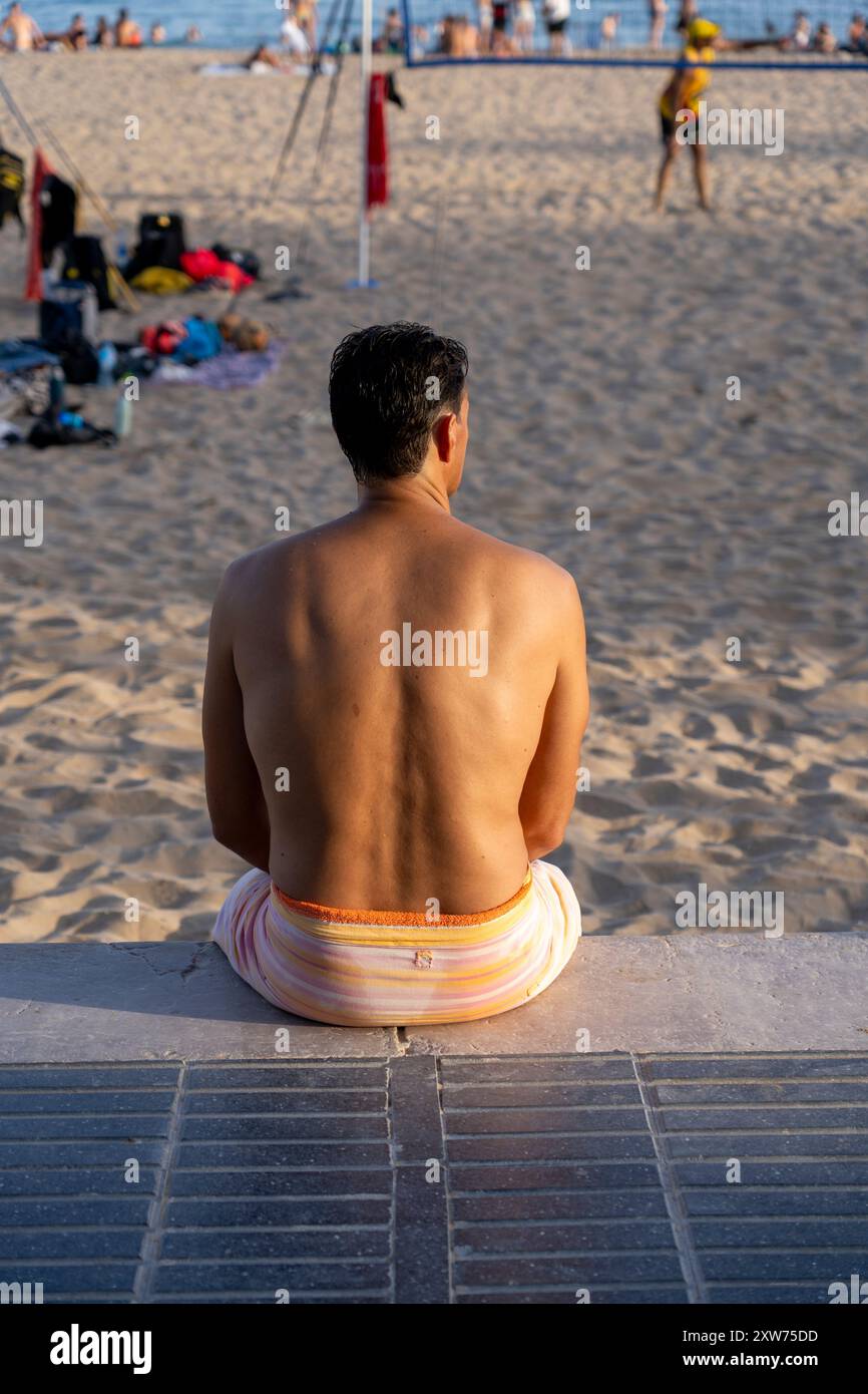Homme assis sur Promenade regardant les gens sur la plage à Sitges, Espagne Banque D'Images