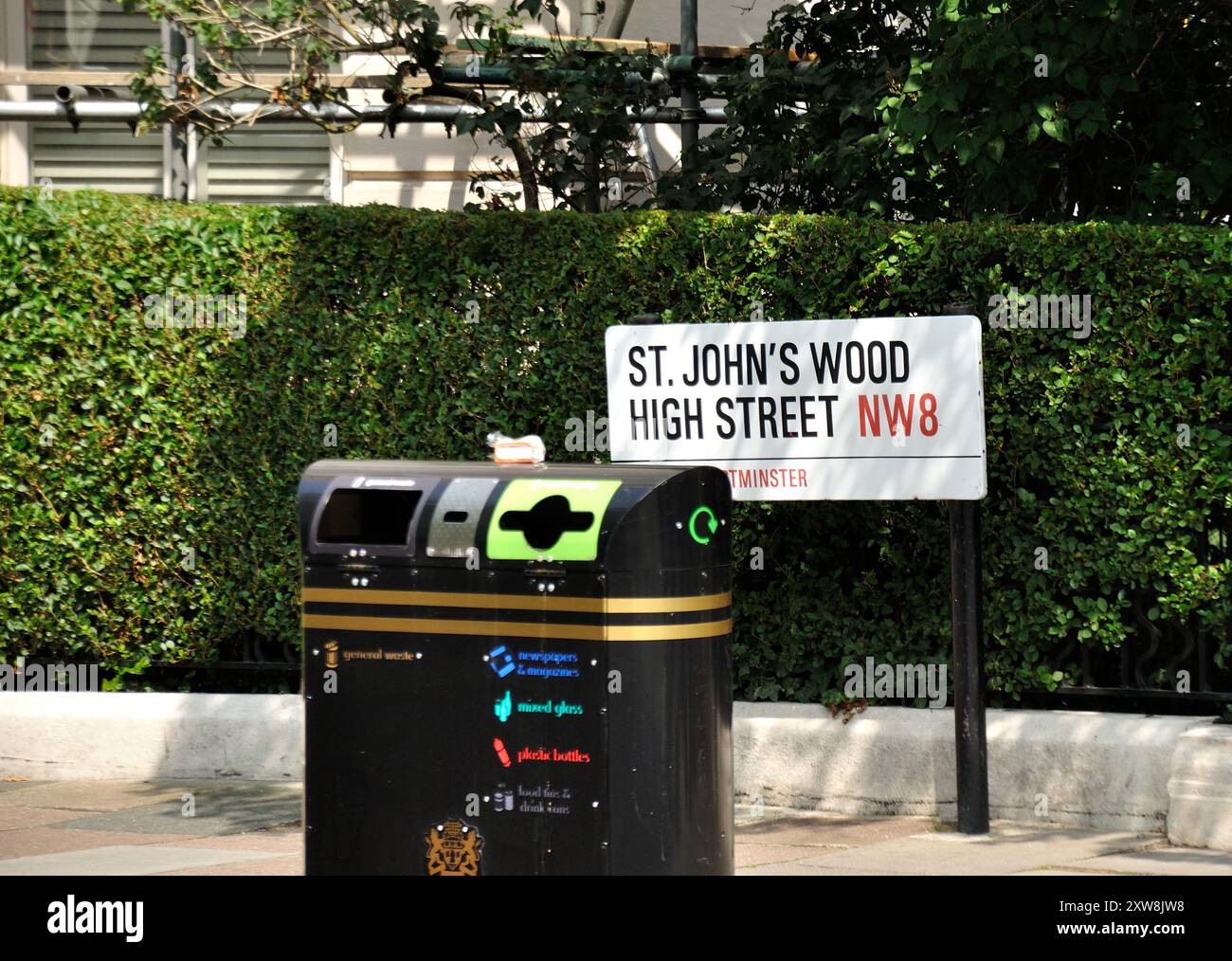 Panneau de rue pour St John's Wood High Street, St John's Wood, Londres, Angleterre, Royaume-Uni, haies, plantes de jardin ; poubelles ; ordures. C'est une très bonne-mère Banque D'Images