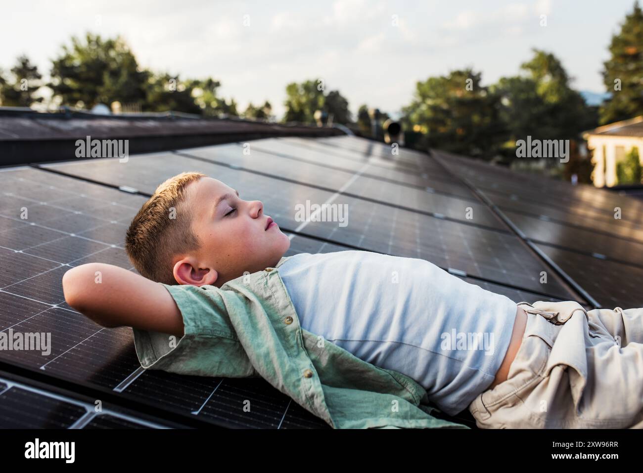 Garçon allongé sur le toit avec des panneaux solaires, les yeux fermés. Installation solaire ou photovoltaïque sur le toit. Un avenir durable pour la prochaine génération. Banque D'Images