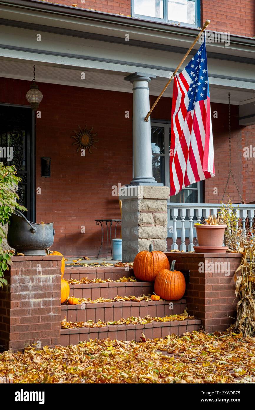 Porche avant d'une maison avec un drapeau des États-Unis, des feuilles d'automne tombées, et un affichage de citrouille d'automne pour Halloween. Banque D'Images