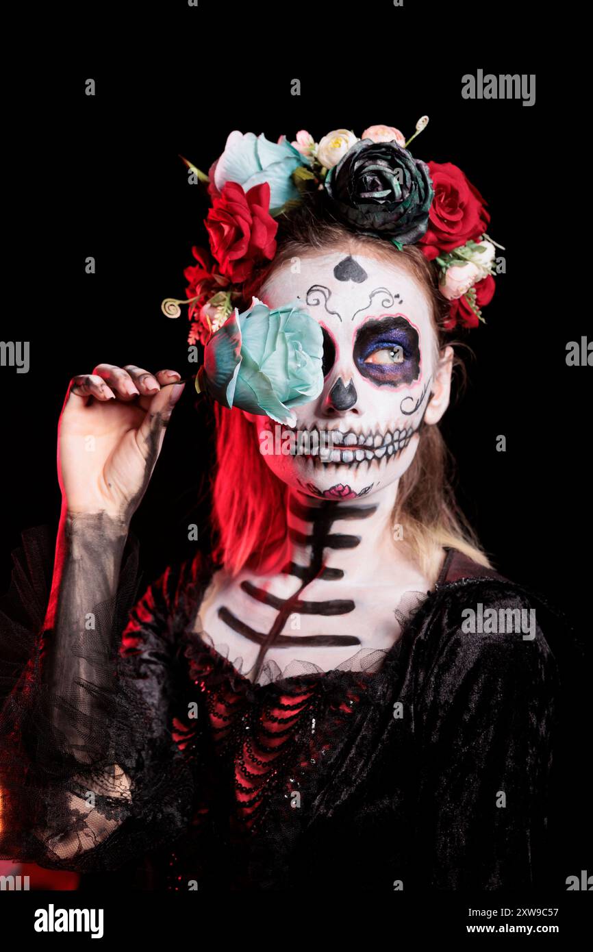 Femme posant avec la rose bleue tout en portant le maquillage squelette et costume d'horreur pour célébrer dios de los muertos pendant Halloween. Dame macabre habillée comme personnage de la Catrina le jour de l'événement mort Banque D'Images