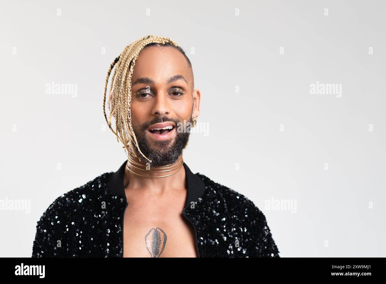 Homme gay noir confiant avec maquillage confus isolé sur fond blanc, veste noire habillée avec des sequins. Dégage un sentiment de fierté et d'individualité. Pouvoir de diversité du style personnel Banque D'Images
