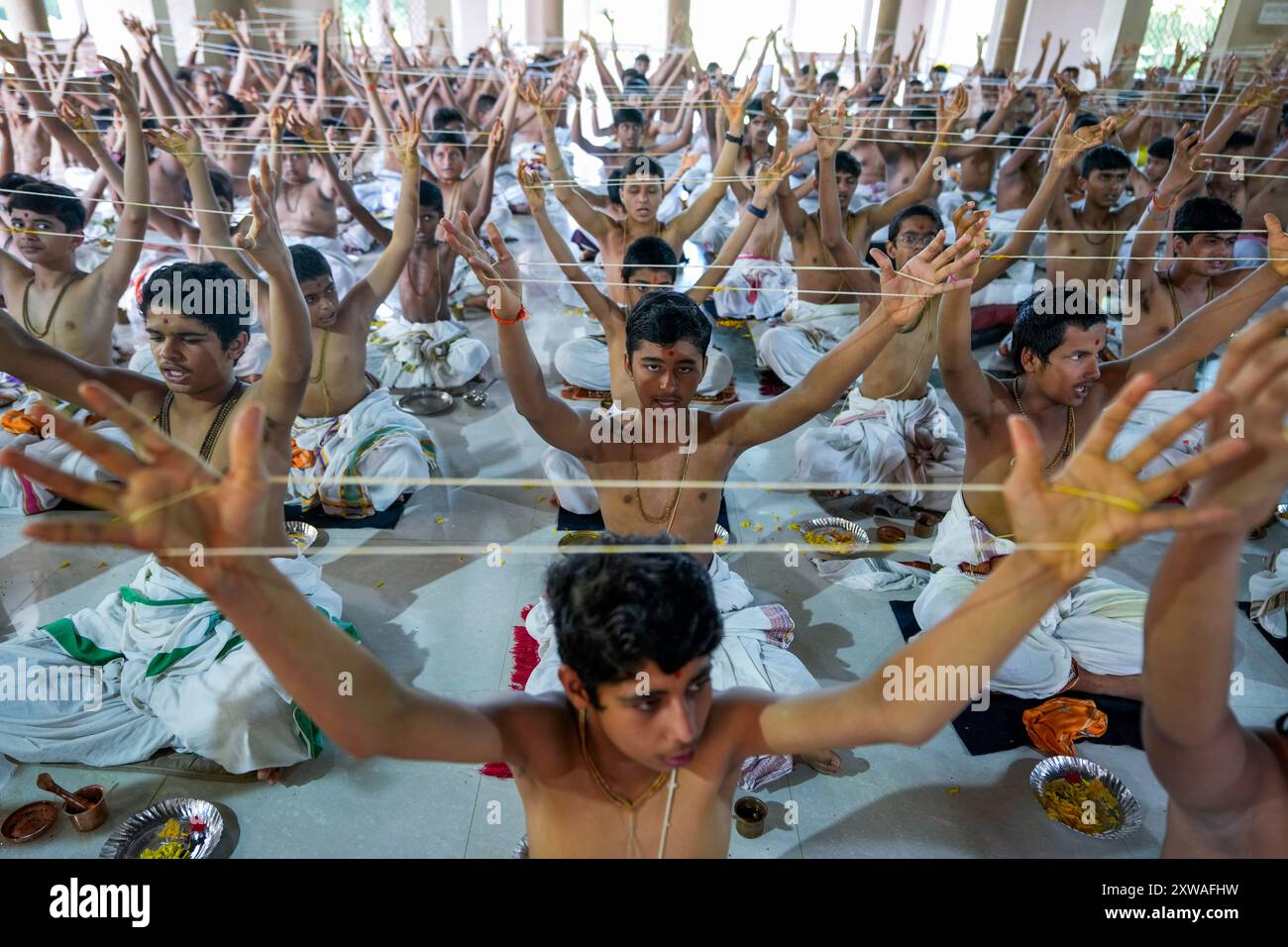Students of the Swaminarayan Gurukul Vishwavidya Pratishthanam (SGVP) perform rituals holding sacred threads, called Janoi, they wear across their bodies, during a change-over ceremony that coincides with Raksha Bandhan festival in Ahmedabad, India, Monday, Aug. 19, 2024. (AP Photo/Ajit Solanki) Banque D'Images
