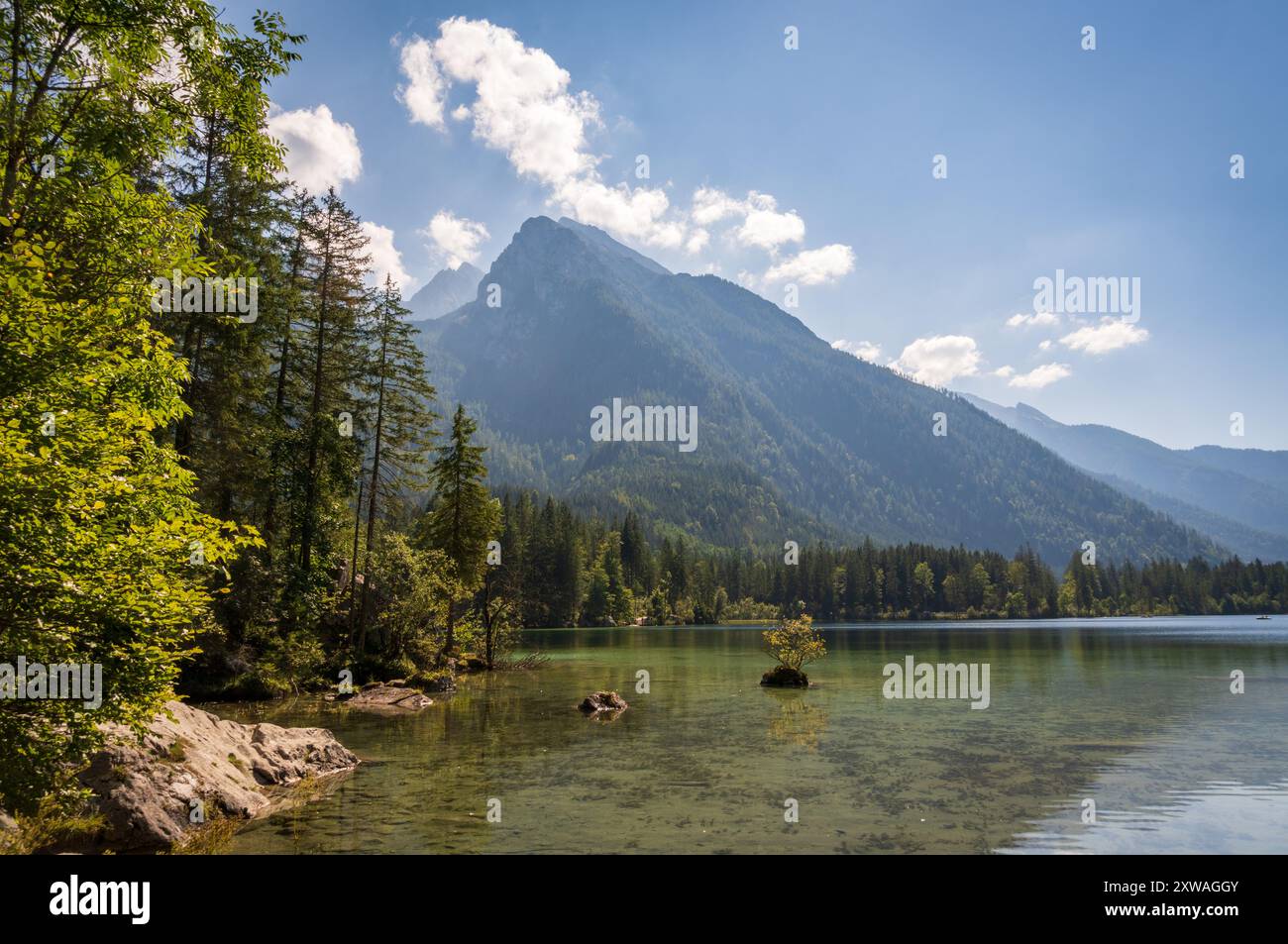 Un lac alpin calme, entouré de forêts, s'étend vers une vallée montagneuse brumeuse, avec une petite barque, près de Ramsau bei Berchtesgaden, en Bavière, Allemagne. Banque D'Images