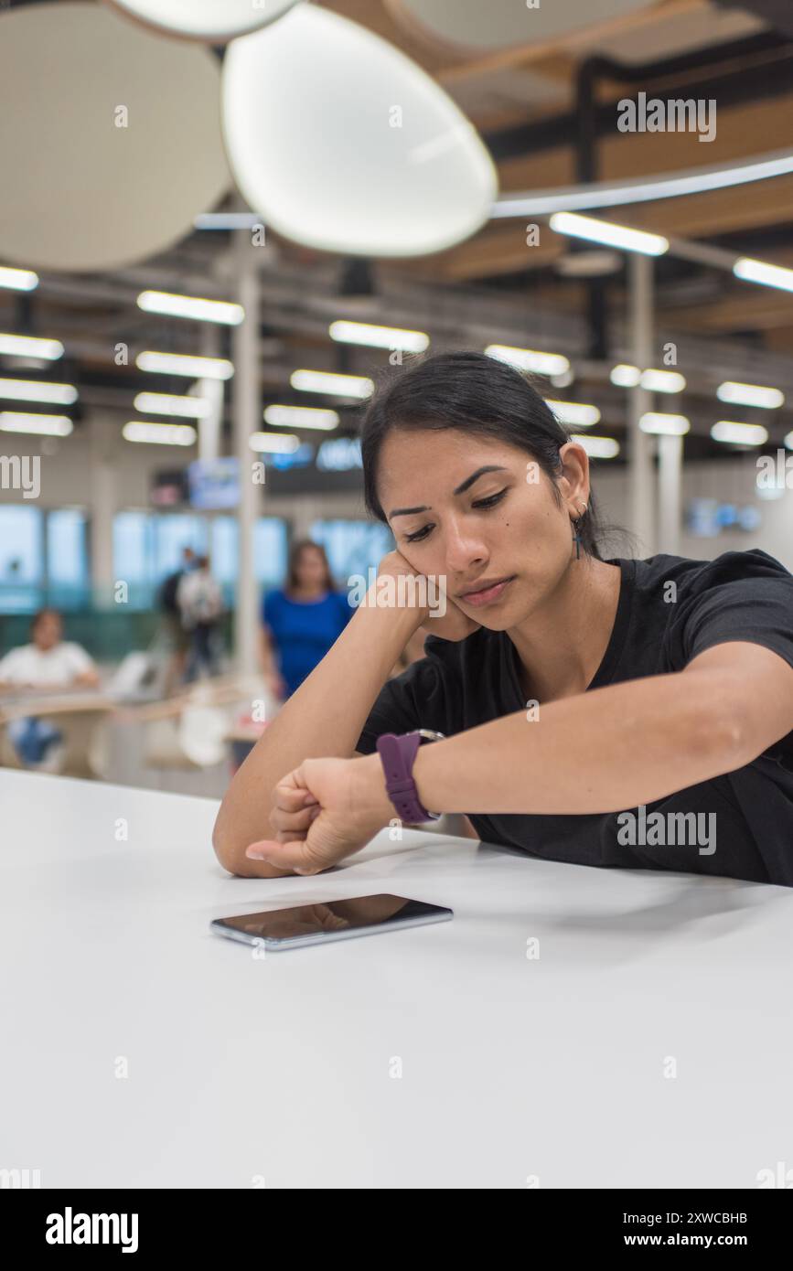 Femme fatiguée d'attendre à l'aéroport en vérifiant sa montre. Banque D'Images