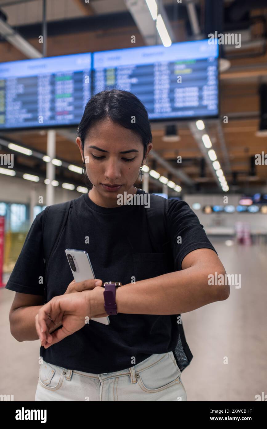 Jeune femme vérifiant le téléphone et la montre intelligente attendant le vol retardé Banque D'Images