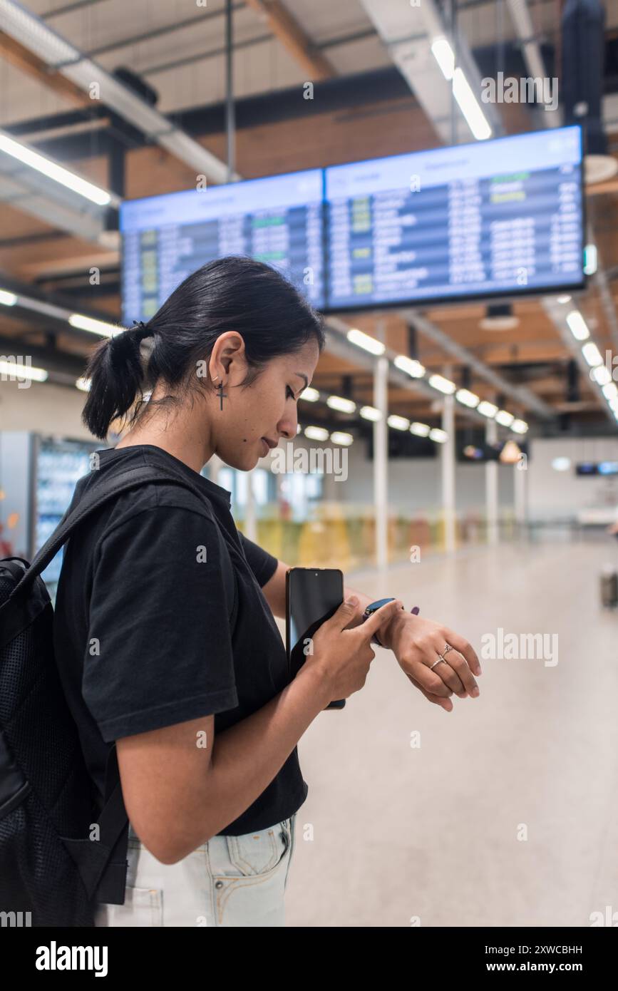 Femme vérifiant le téléphone et smartwatch attendant le vol retardé Banque D'Images