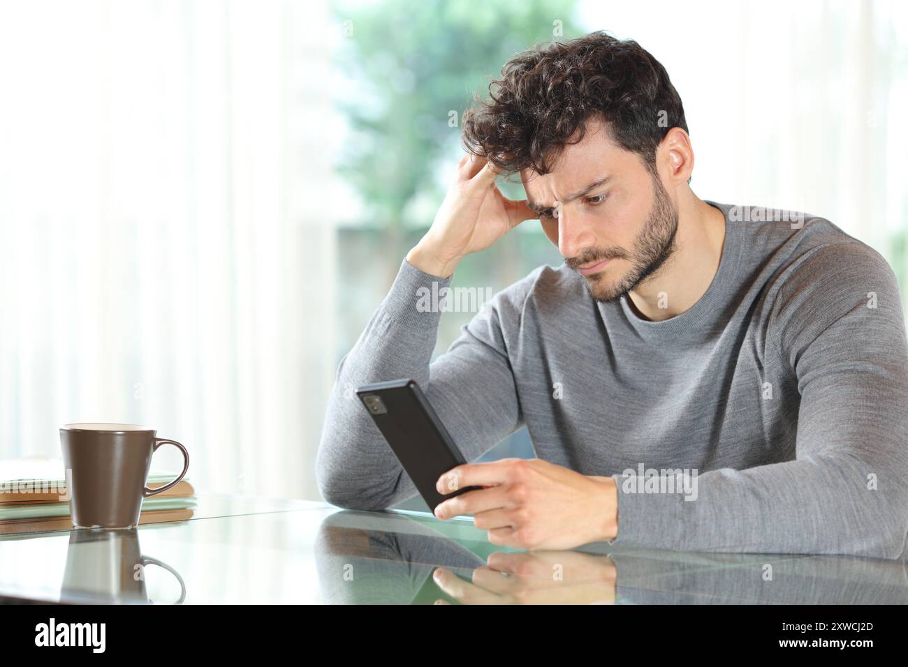 Homme inquiet vérifiant le téléphone portable assis à la maison Banque D'Images