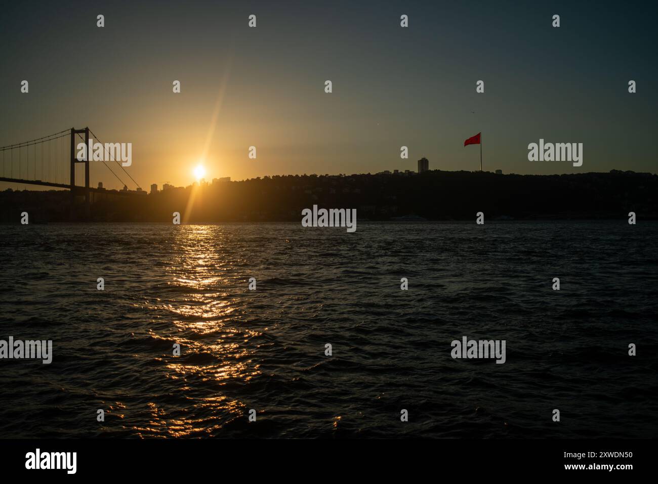 Une vue imprenable sur le Bosphore d'Istanbul au coucher du soleil, avec l'emblématique drapeau turc agitant fièrement. La lumière dorée se reflète sur l'eau, hig Banque D'Images Une vue imprenable sur le Bosphore d'Istanbul au coucher du soleil, avec l'emblématique drapeau turc agitant fièrement. La lumière dorée se reflète sur l'eau, hig Banque D'Images