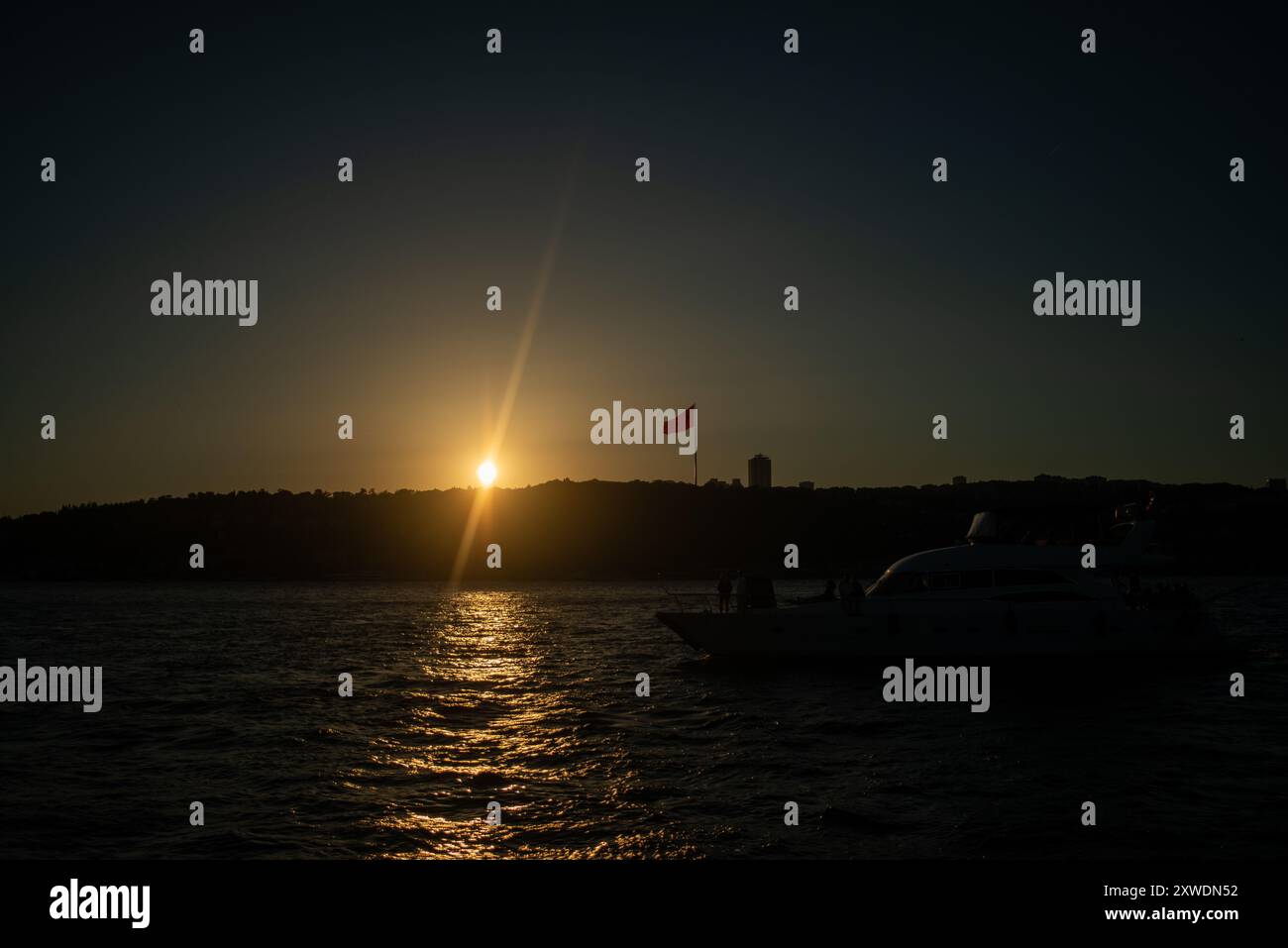 Une vue imprenable sur le Bosphore d'Istanbul au coucher du soleil, avec l'emblématique drapeau turc agitant fièrement. La lumière dorée se reflète sur l'eau, hig Banque D'Images Une vue imprenable sur le Bosphore d'Istanbul au coucher du soleil, avec l'emblématique drapeau turc agitant fièrement. La lumière dorée se reflète sur l'eau, hig Banque D'Images