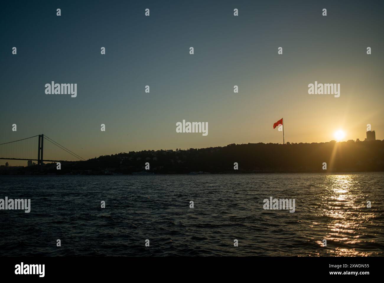 Une vue imprenable sur le Bosphore d'Istanbul au coucher du soleil, avec l'emblématique drapeau turc agitant fièrement. La lumière dorée se reflète sur l'eau, hig Banque D'Images Une vue imprenable sur le Bosphore d'Istanbul au coucher du soleil, avec l'emblématique drapeau turc agitant fièrement. La lumière dorée se reflète sur l'eau, hig Banque D'Images