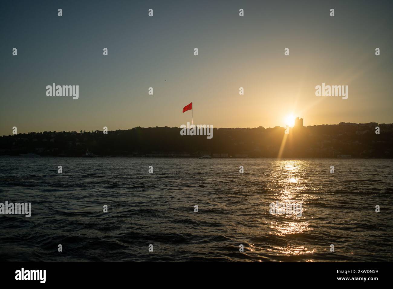 Une vue imprenable sur le Bosphore d'Istanbul au coucher du soleil, avec l'emblématique drapeau turc agitant fièrement. La lumière dorée se reflète sur l'eau, hig Banque D'Images Une vue imprenable sur le Bosphore d'Istanbul au coucher du soleil, avec l'emblématique drapeau turc agitant fièrement. La lumière dorée se reflète sur l'eau, hig Banque D'Images