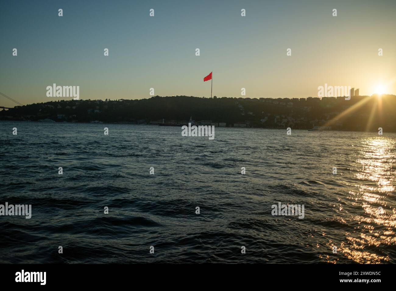 Une vue imprenable sur le Bosphore d'Istanbul au coucher du soleil, avec l'emblématique drapeau turc agitant fièrement. La lumière dorée se reflète sur l'eau, hig Banque D'Images Une vue imprenable sur le Bosphore d'Istanbul au coucher du soleil, avec l'emblématique drapeau turc agitant fièrement. La lumière dorée se reflète sur l'eau, hig Banque D'Images