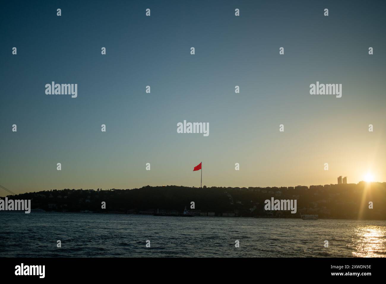 Une vue imprenable sur le Bosphore d'Istanbul au coucher du soleil, avec l'emblématique drapeau turc agitant fièrement. La lumière dorée se reflète sur l'eau, hig Banque D'Images Une vue imprenable sur le Bosphore d'Istanbul au coucher du soleil, avec l'emblématique drapeau turc agitant fièrement. La lumière dorée se reflète sur l'eau, hig Banque D'Images