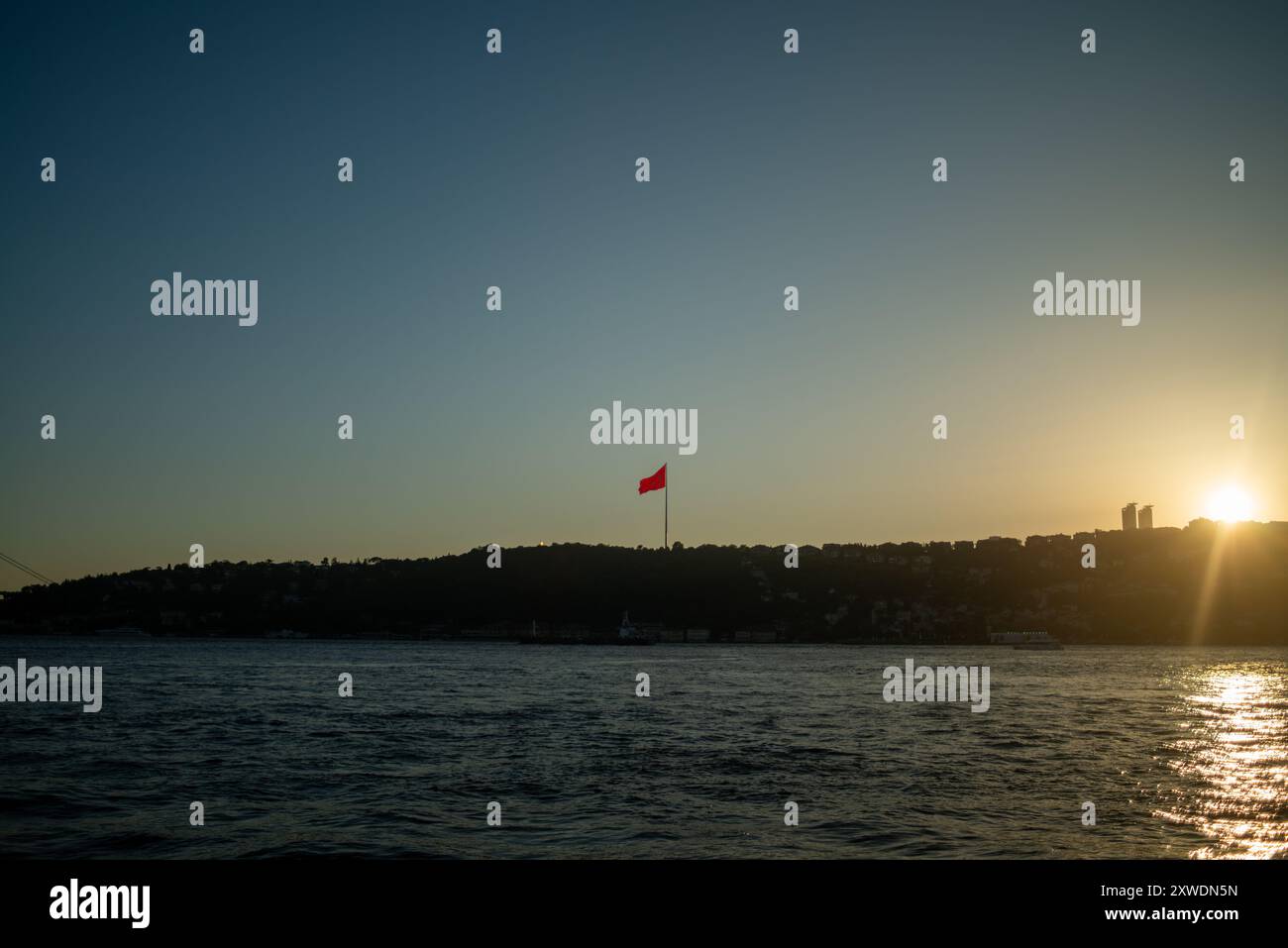 Une vue imprenable sur le Bosphore d'Istanbul au coucher du soleil, avec l'emblématique drapeau turc agitant fièrement. La lumière dorée se reflète sur l'eau, hig Banque D'Images Une vue imprenable sur le Bosphore d'Istanbul au coucher du soleil, avec l'emblématique drapeau turc agitant fièrement. La lumière dorée se reflète sur l'eau, hig Banque D'Images
