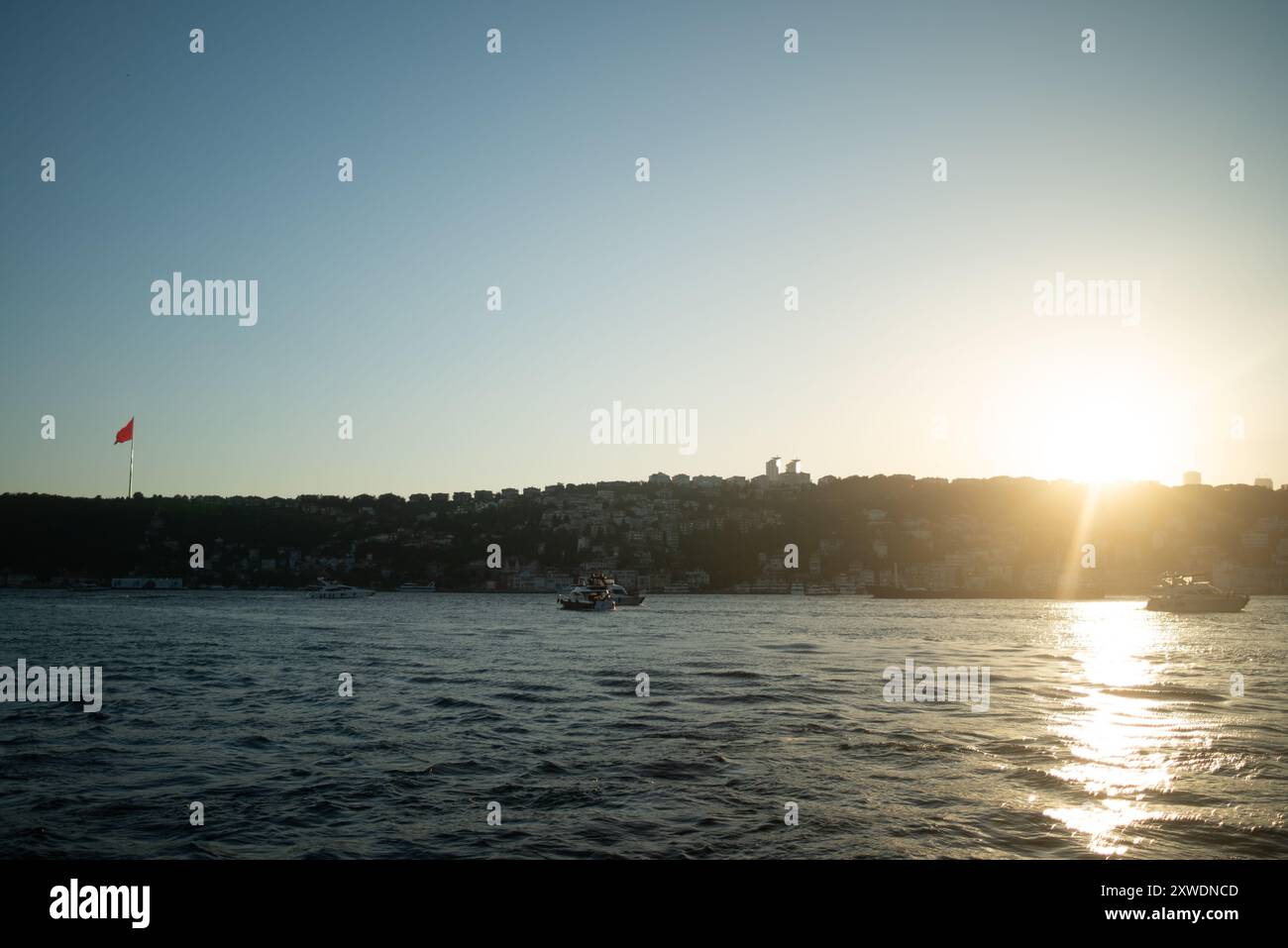 Une vue imprenable sur le Bosphore d'Istanbul au coucher du soleil, avec l'emblématique drapeau turc agitant fièrement. La lumière dorée se reflète sur l'eau, hig Banque D'Images Une vue imprenable sur le Bosphore d'Istanbul au coucher du soleil, avec l'emblématique drapeau turc agitant fièrement. La lumière dorée se reflète sur l'eau, hig Banque D'Images