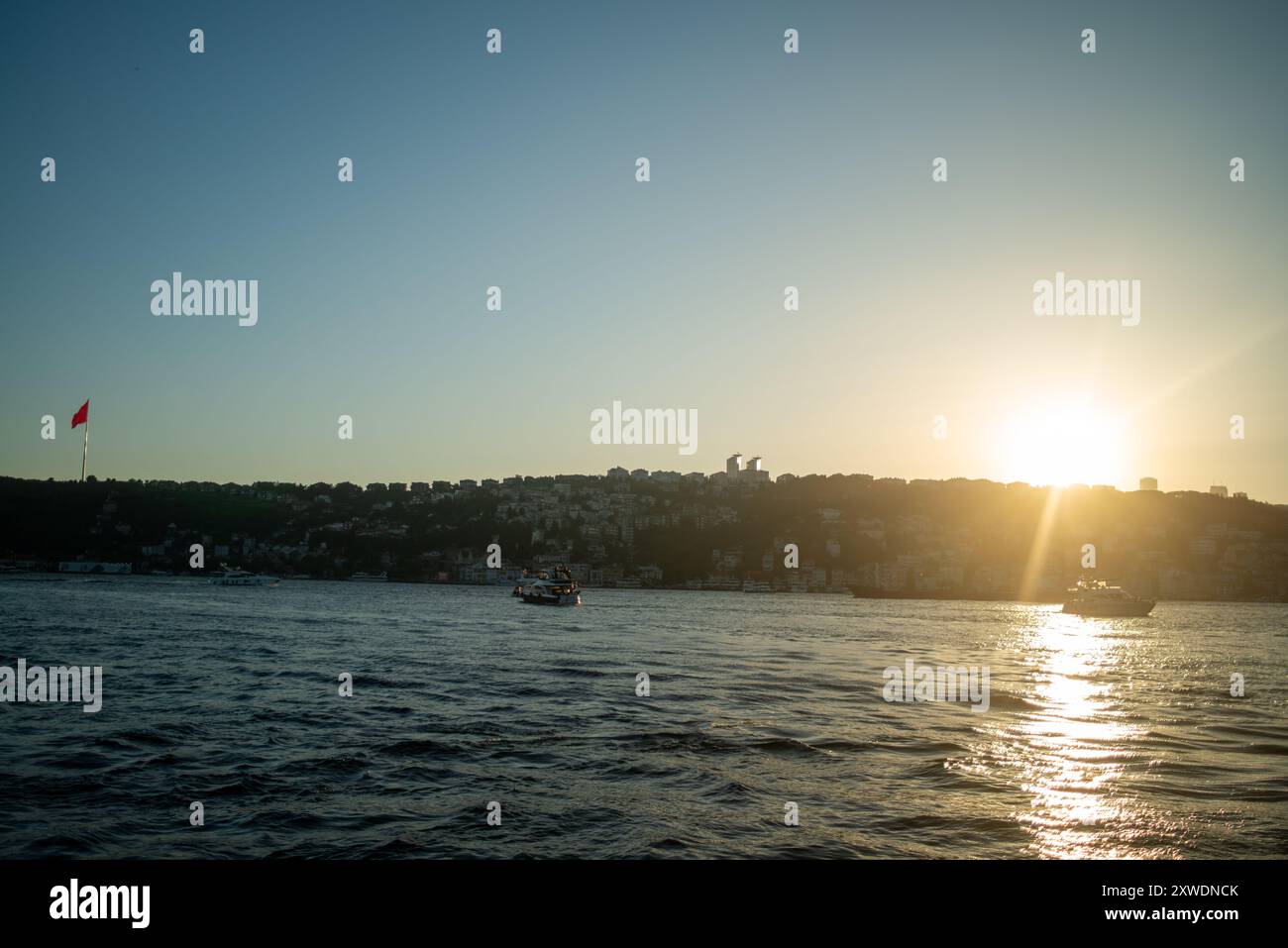 Une vue imprenable sur le Bosphore d'Istanbul au coucher du soleil, avec l'emblématique drapeau turc agitant fièrement. La lumière dorée se reflète sur l'eau, hig Banque D'Images Une vue imprenable sur le Bosphore d'Istanbul au coucher du soleil, avec l'emblématique drapeau turc agitant fièrement. La lumière dorée se reflète sur l'eau, hig Banque D'Images