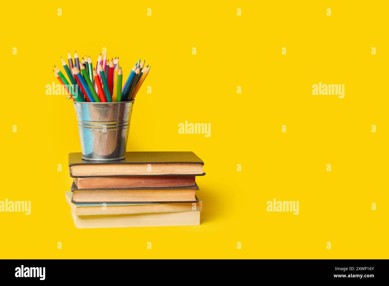 Un seau avec des crayons de couleur sur des livres sur un fond jaune avec espace de copie Banque D'Images