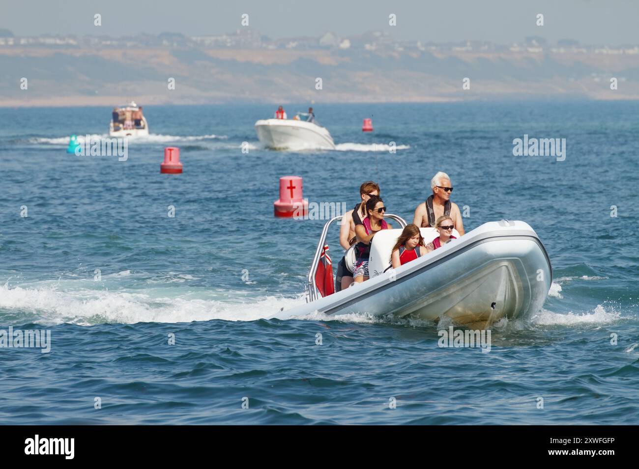 Famille sur Une nervure gonflable rigide, suivie par des bateaux à moteur naviguant sur les bouées marquant le canal d'entrée du port de Christchurch, Royaume-Uni Banque D'Images