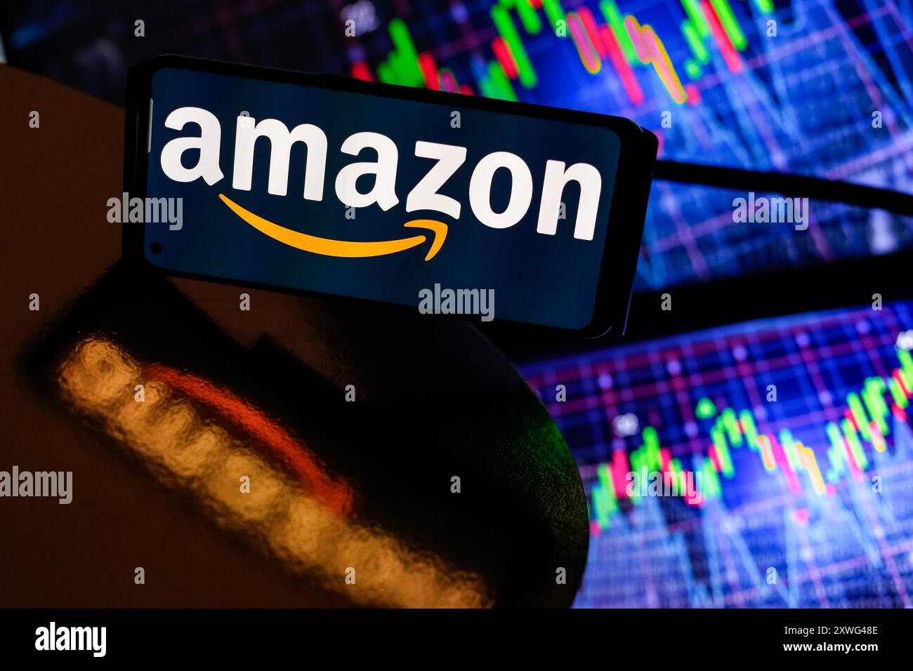 Dans cette illustration photo, le logo Amazon est affiché sur un écran de smartphone contre un écran d'ordinateur ce qui affiche des graphiques boursiers le 19 août 2024 alors que les marchés boursiers se stabilisent après un revers au début du mois d'août. Banque D'Images