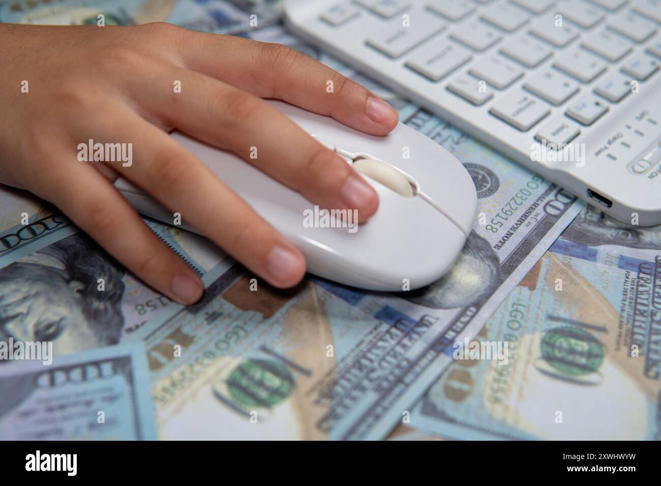Gros plan d'une main tenant une souris d'ordinateur, survolant un lit de billets en dollars américains. Commerce en ligne, payer par clic, transaction numérique Banque D'Images