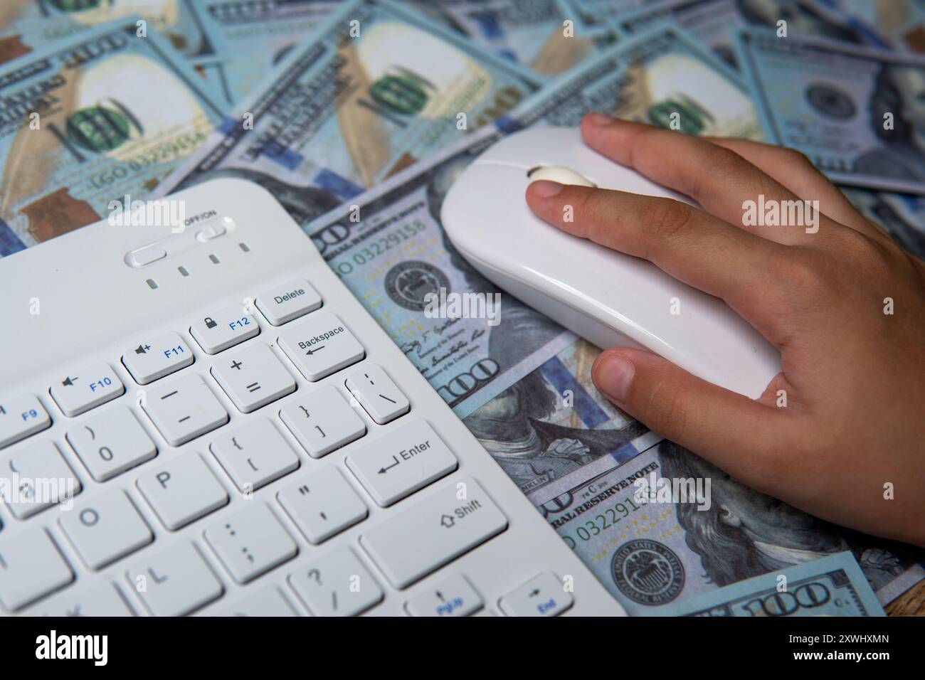 Gros plan d'une main tenant une souris d'ordinateur, survolant un lit de billets en dollars américains. Commerce en ligne, payer par clic, transaction numérique Banque D'Images
