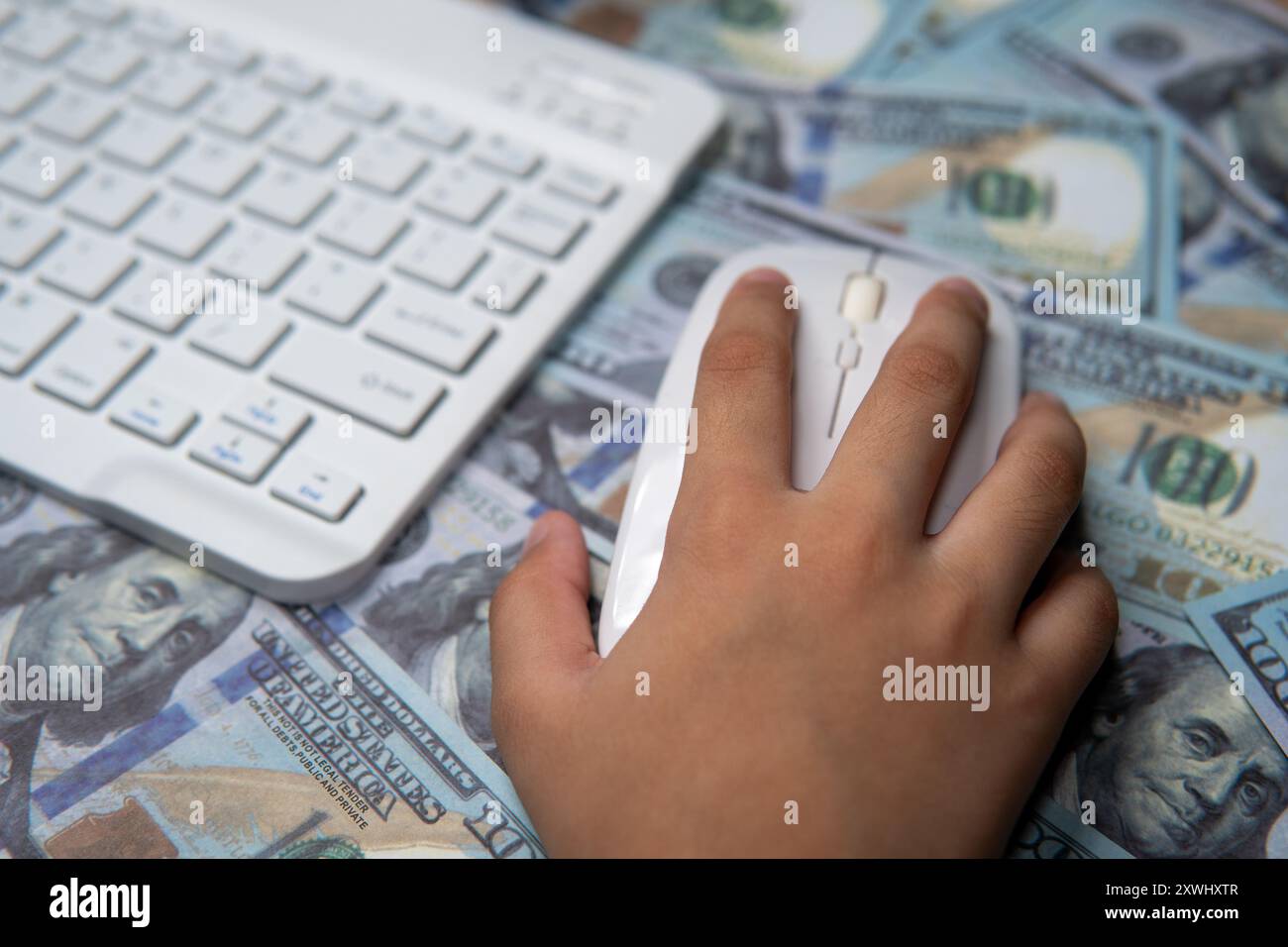 Gros plan d'une main tenant une souris d'ordinateur, survolant un lit de billets en dollars américains. Commerce en ligne, payer par clic, transaction numérique Banque D'Images