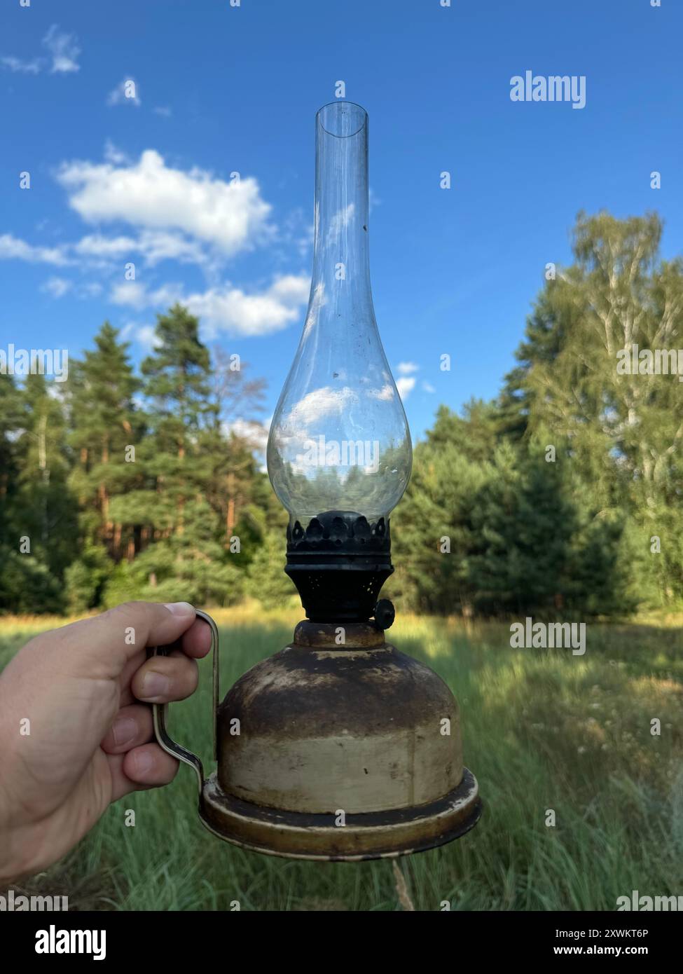 Une vieille lampe à kérosène dans la main d'un homme. Sur fond de forêt et de ciel bleu. Gros plan. Banque D'Images