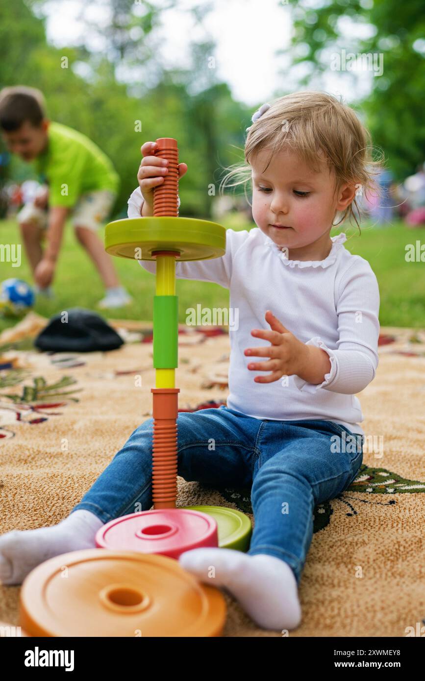 Petite fille jouant avec le jouet puzzle. Image portrait de 2-3 enfant en bas âge. Fille heureuse de l'enfant jouant le jouet de blocs en plastique dans le parc. Banque D'Images