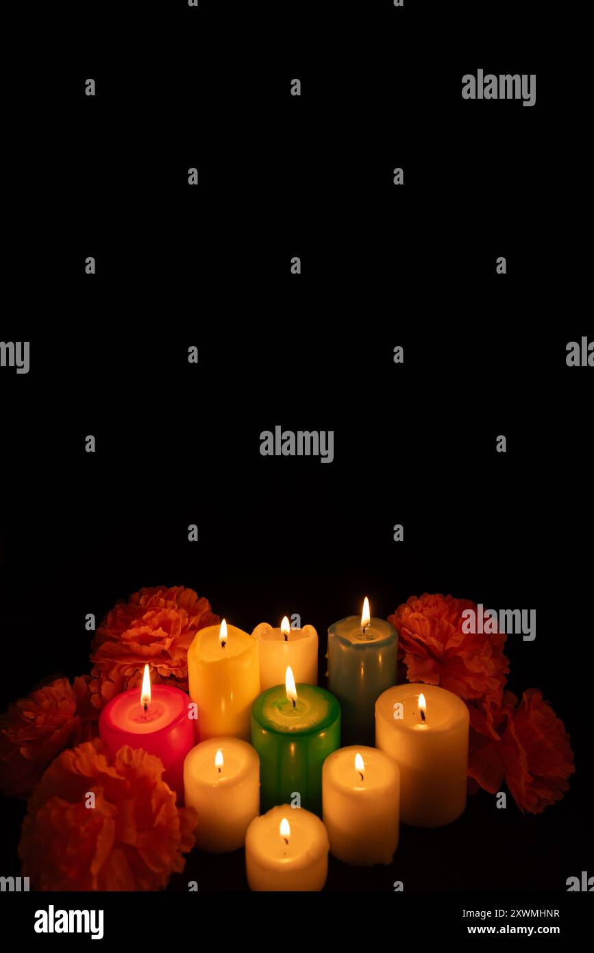 Plan vertical représentant un groupe de bougies allumées entourées de fleurs de souci éclatantes au centre de l'image. Le fond noir est légèrement illum Banque D'Images
