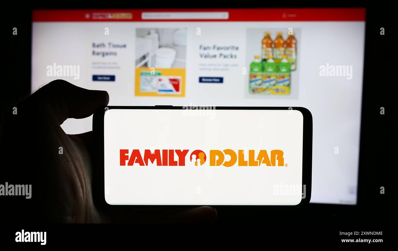 Personne tenant le téléphone portable avec le logo de la société américaine de magasin de variété Family Dollar Stores Inc en face de la page Web de l'entreprise. Concentrez-vous sur l'affichage du téléphone. Banque D'Images