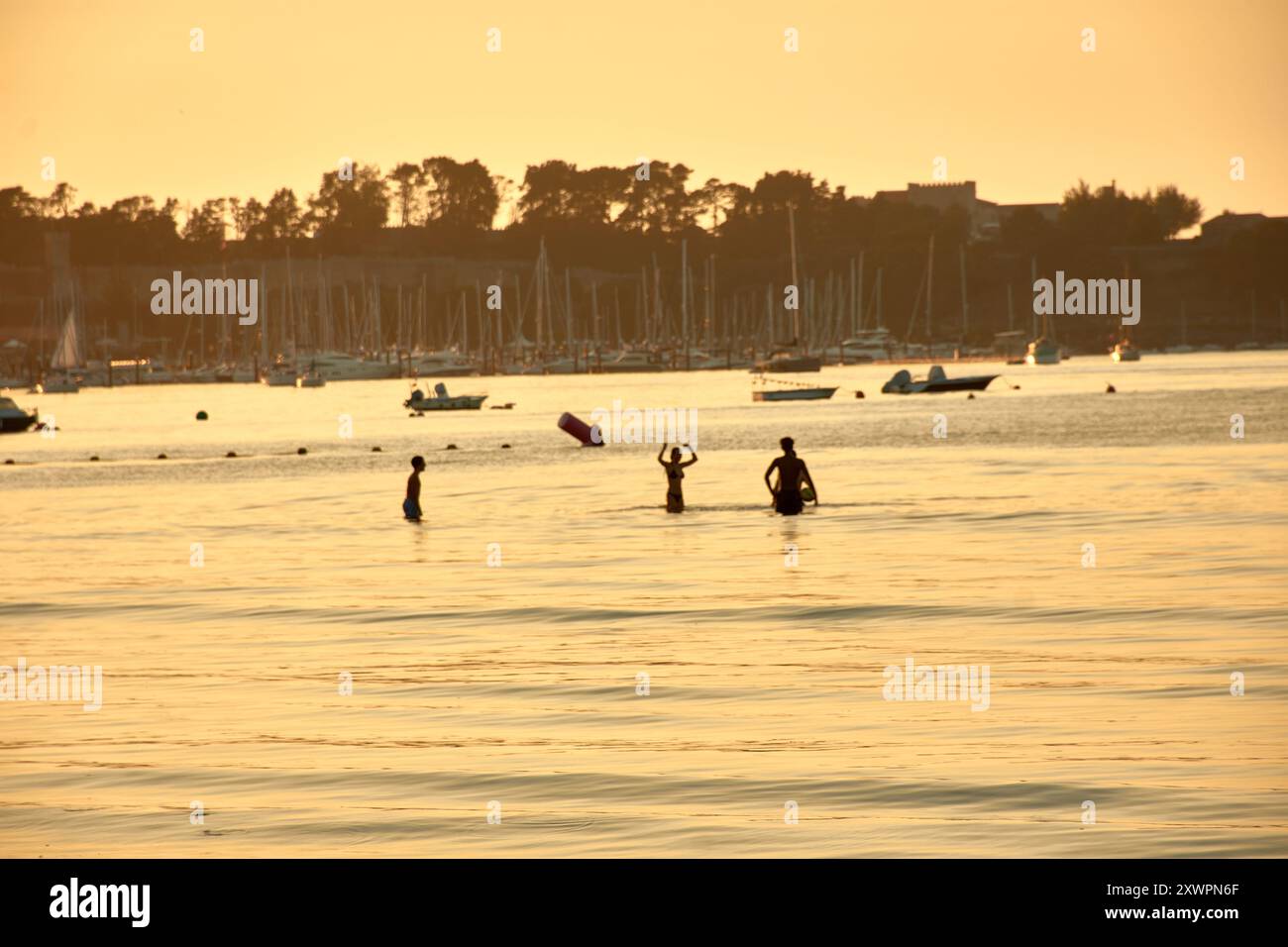 Alors que le jour s’estompe dans la nuit, les silhouettes des jeunes jouant et se baignant dans les eaux de la plage de Ladeira créent un sce captivant et nostalgique Banque D'Images