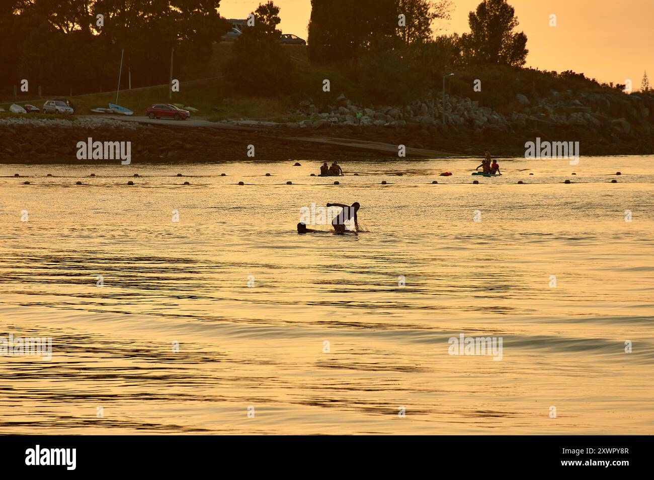 Alors que le jour s’estompe dans la nuit, les silhouettes des jeunes jouant et se baignant dans les eaux de la plage de Ladeira créent un sce captivant et nostalgique Banque D'Images