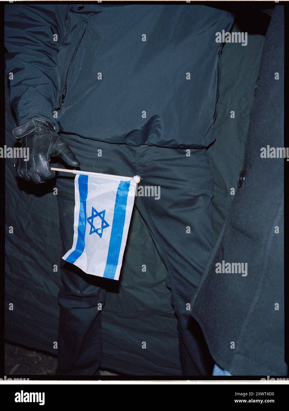 Un manifestant vêtu de vêtements sombres tient un petit drapeau israélien lors d'une manifestation organisée par Antideutschen à Berlin. L'image capture un sentiment de défi et d'expression politique dans une atmosphère tendue. Banque D'Images