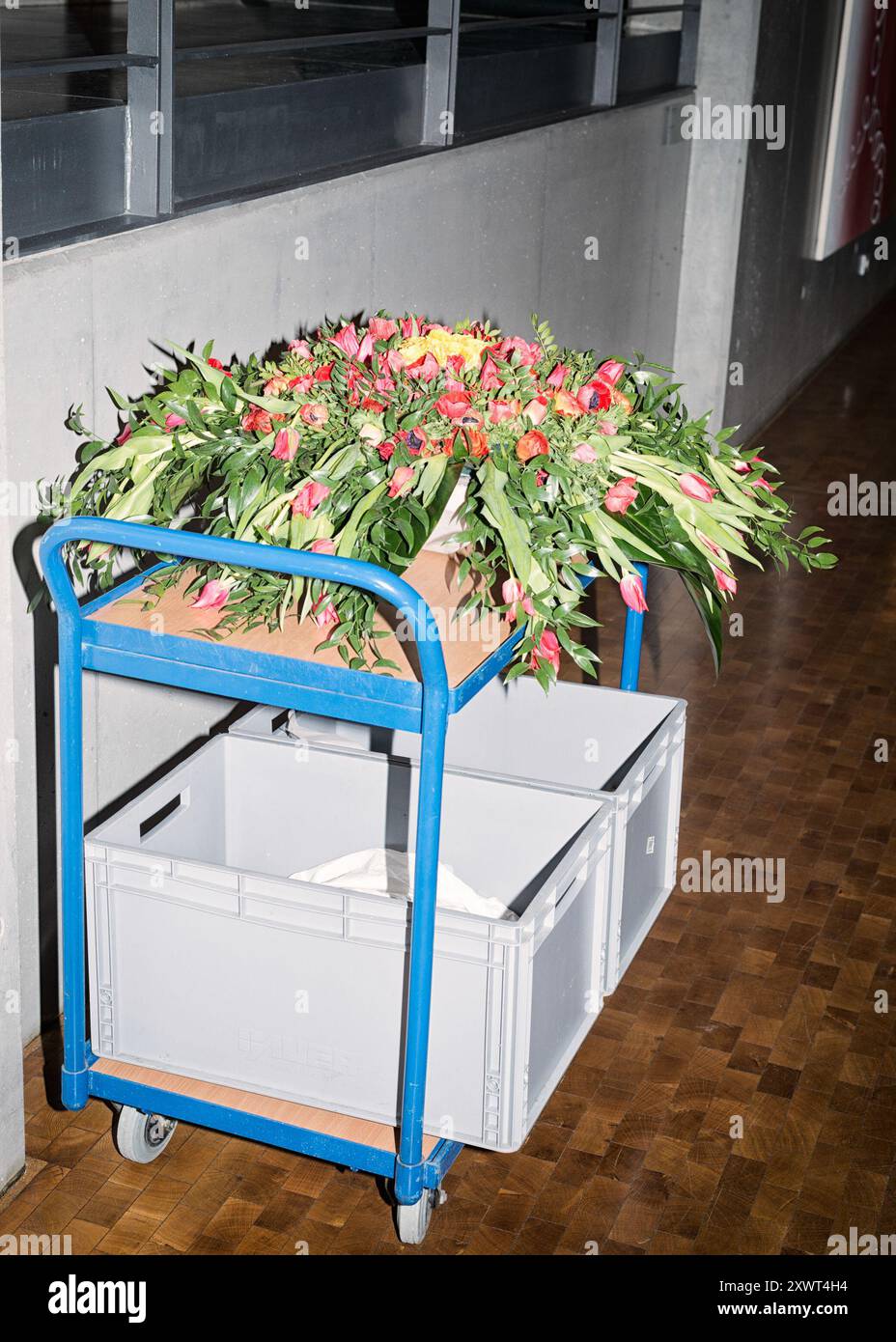 Un bouquet vibrant de fleurs repose sur un chariot utilitaire bleu dans un environnement industriel, symbolisant un contraste entre la nature et les machines. Les fleurs ajoutent de la couleur et de la vie à l'espace autrement sombre. Banque D'Images