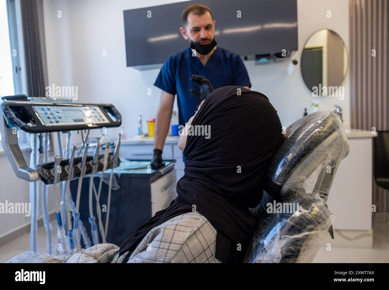 Conversation entre un dentiste et une femme musulmane portant le hijab regardant ses dents radiographie à l'écran et le médecin décrit son traitement Banque D'Images
