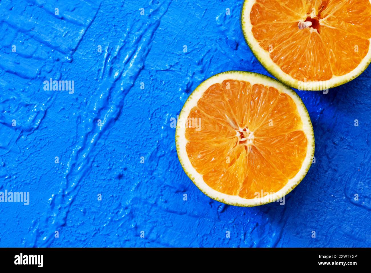 Deux parties d'une orange en diagonale dans le coin inférieur gauche sur une table bleue. Banque D'Images