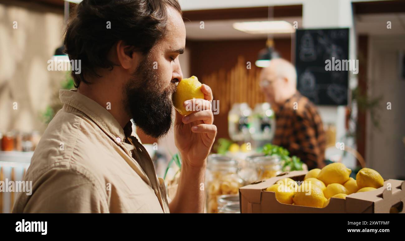 Homme dans les magasins de magasin zéro déchet pour les fruits cultivés à la ferme, obtenant la dopamine précipitée tout en les sentant. Le client fait l'expérience d'un bonheur nostalgique de l'enfance tout en ressentant un agréable arôme de citron dans un magasin local, zoom avant plan Banque D'Images