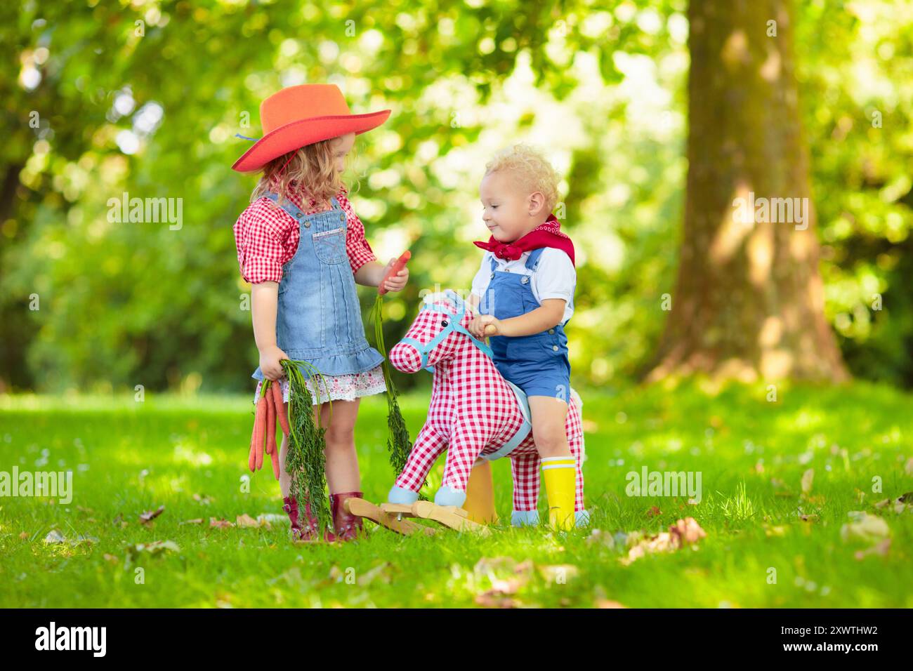 Petit garçon et fille habillés comme cow-boy et cow-girl jouant avec jouet cheval à bascule dans le parc. Les enfants jouent à l'extérieur. Enfants en costumes d'Halloween Banque D'Images